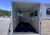 Open horse trailer interior with stalls, wood panels, and side windows under a bright blue sky.