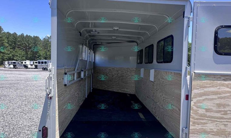 Open horse trailer interior with stalls, wood panels, and side windows under a bright blue sky.