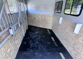 Interior of a white enclosed trailer with plywood walls, metal gate on the left, and windows along the right wall.