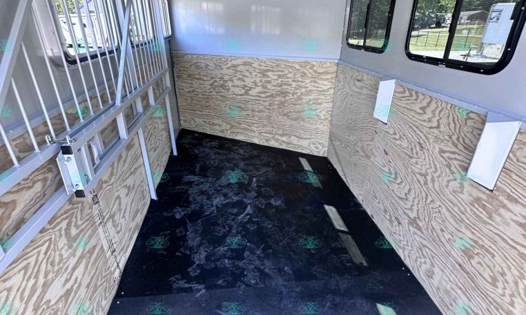 Interior of a white enclosed trailer with plywood walls, metal gate on the left, and windows along the right wall.