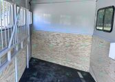 Interior of a blank horse trailer with plywood walls and a divider gate on the left side.