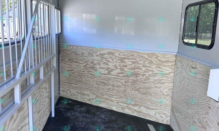 Interior of a blank horse trailer with plywood walls and a divider gate on the left side.