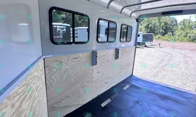 Interior of a light gray trailer with plywood walls, windows along the side, and a dark rubber floor, seen from the open rear doorway.