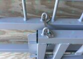 Close-up of a trailer hitch lock securing the coupling on a gray trailer frame near a wooden deck.