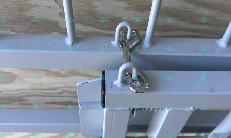 Close-up of a trailer hitch lock securing the coupling on a gray trailer frame near a wooden deck.