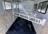 Interior of a horse trailer with a white metal divider, plywood walls, and windows along the sides for ventilation and visibility.