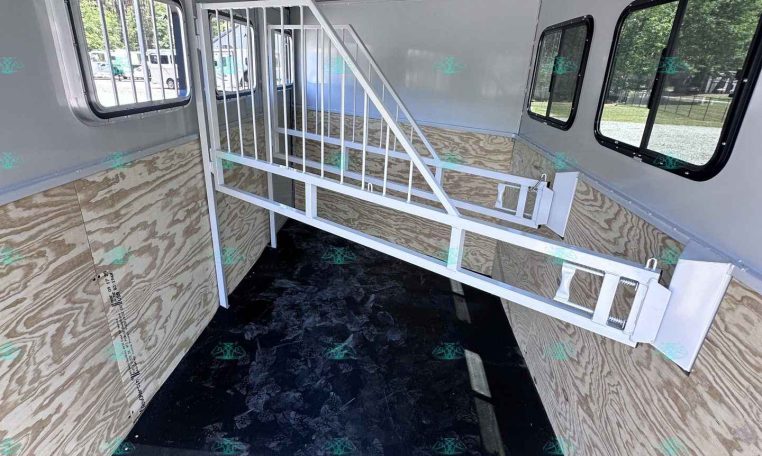 Interior of a horse trailer with a white metal divider, plywood walls, and windows along the sides for ventilation and visibility.