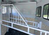 Interior of a gray horse trailer with a metal staircase, partition stall, and windows along the side wall.