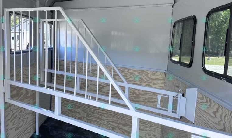 Interior of a gray horse trailer with a metal staircase, partition stall, and windows along the side wall.