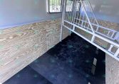 Interior of a box trailer with plywood walls, black rubber floor, and white metal ramp gate folded inside.