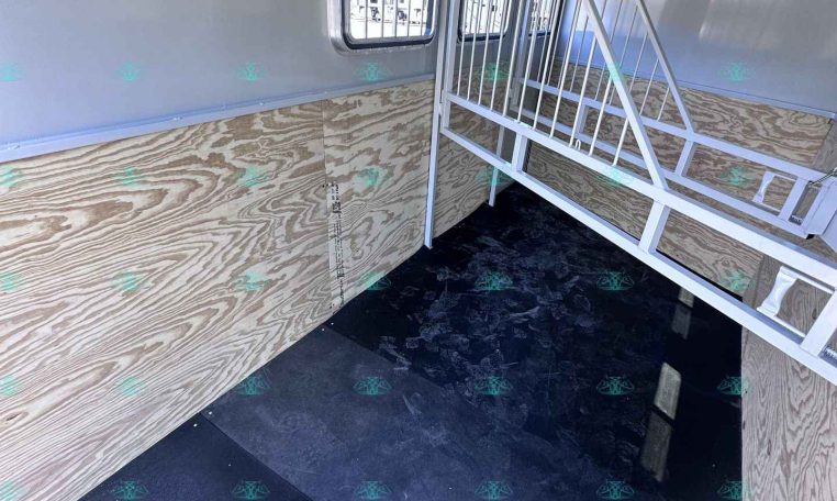 Interior of a box trailer with plywood walls, black rubber floor, and white metal ramp gate folded inside.