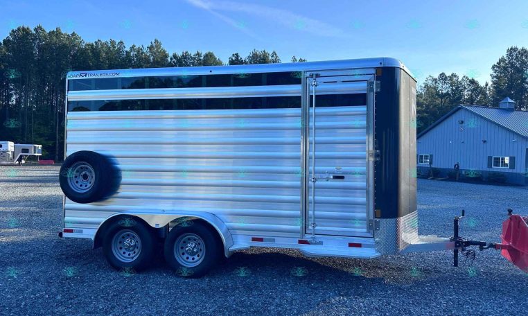 Polished aluminum livestock trailer with three axles and a side access door on a gravel lot, watermarked CarolinaTrailerSales.com