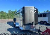 Shiny silver cargo trailer with diamond‑plate front and 'M Trailers' logo, parked on a gravel lot with a blue sky.
