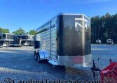 Large black enclosed horse trailer with chrome diamond-plate front, parked in a gravel lot among other trailers, trees in the background.