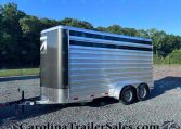 Side view of a silver enclosed cargo trailer on a gravel lot with trees and a clear blue sky behind it.