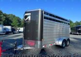 Large aluminum trailer with a black front panel and chrome diamond-plate lower edge, parked with other trailers on a gravel lot under a blue sky.