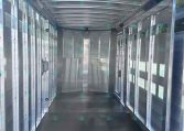 Interior view of a silver aluminum cargo trailer with side doors and a dark floor, rear opening visible ahead.