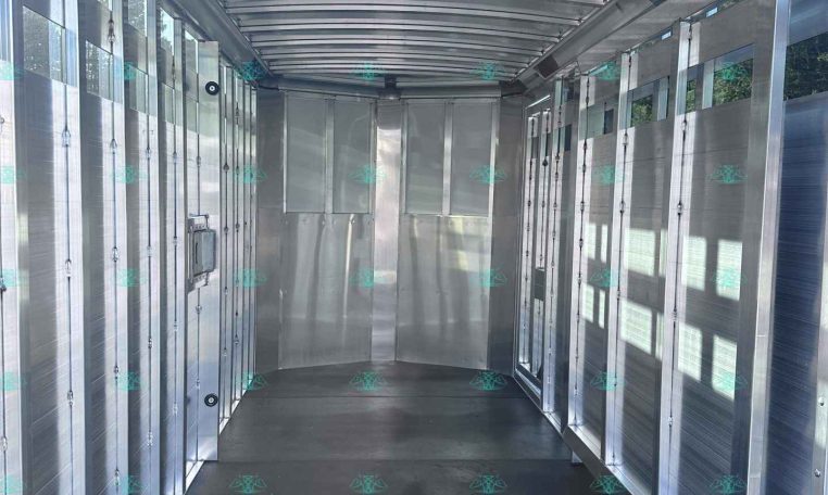 Interior view of a silver aluminum cargo trailer with side doors and a dark floor, rear opening visible ahead.