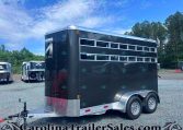 Black horse trailer with multiple horizontal windows, parked in a gravel lot with other trailers and trees in the background.