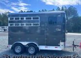 Side view of a dark gray horse trailer with windows and a door, parked on a gravel lot with trees in the background; branding along the top edge reads Bar M Trailers.com.