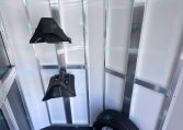 Interior of a metal trailer with a spare tire on the floor and two black plastic saddle-like mounts attached to the wall/rack above them.