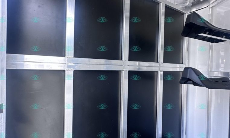 Inside a silver horse trailer with black divider panels and a row of metal hooks along the top for tack storage.