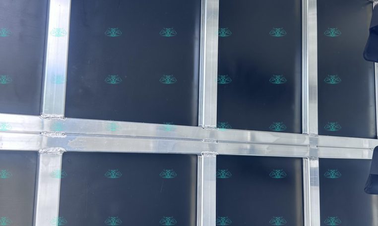 Interior of a trailer with blue wall panels, silver framing, and a row of metal hooks along the ceiling for securing gear.