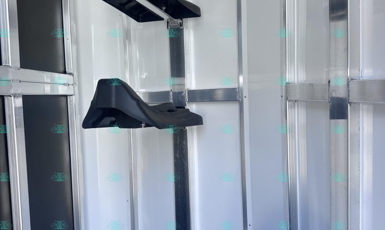 Interior of a metal trailer showing wall-mounted black plastic brackets and a spare tire in the corner