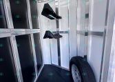 Interior of a metal trailer cargo area with black padded partition panels and a mounted wheel, hanging hooks along the ceiling, and a spare tire at the corner.