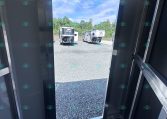 Interior of a metal trailer with the rear door open, revealing two horse trailers parked on a gravel lot under a blue sky.