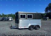 Black and silver trailer with two windows on a gravel lot, surrounded by other trailers under a clear blue sky.