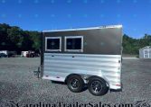 Black and silver two-window trailer parked on a gravel lot with a blue sky and trees in the background.