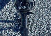 Close-up of a trailer hitch with a vertical jack, safety chains, and coiled cables on gray gravel.