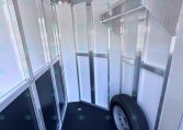 Interior of a silver aluminum trailer showing framing, panels, and a mounted spare wheel in the corner (empty storage space).