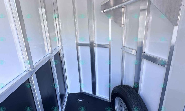 Interior of a silver aluminum trailer showing framing, panels, and a mounted spare wheel in the corner (empty storage space).