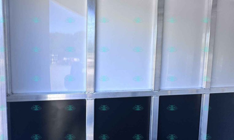 Interior of a metal-framed trailer wall with vertical studs and glossy gray panels along the sides, plus a row of hooks near the ceiling