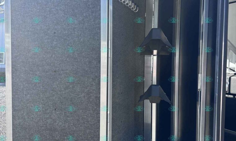 Interior of a metal trailer with gray felt walls, coat hooks along the wall, and vertical garment rails for hanging items.