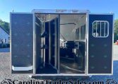 Open horse trailer with interior stalls and tack hooks, parked on a gravel lot.