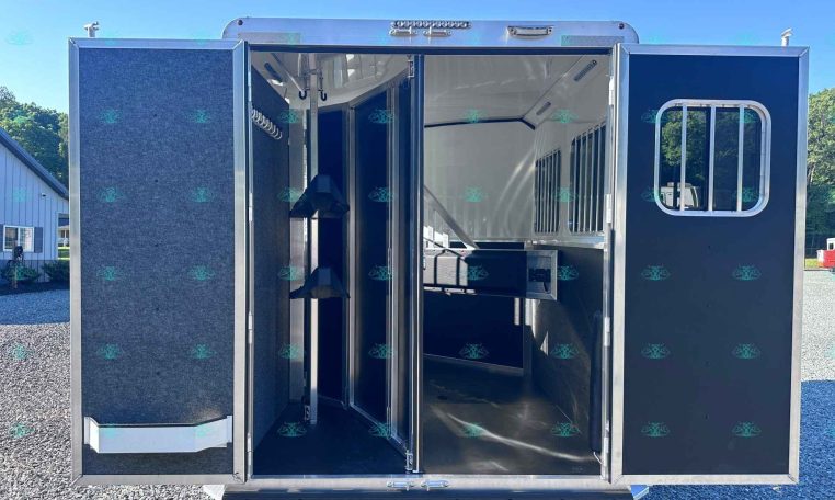 Open horse trailer with interior stalls and tack hooks, parked on a gravel lot.