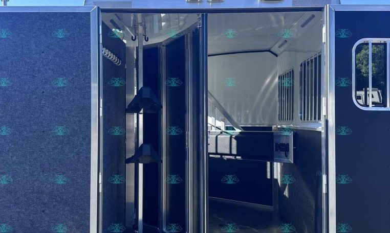 Open horse trailer with interior stalls and partition rails, blue exterior, parked on gravel.
