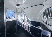 Interior of a white horse trailer with a partitioned stall, steps, and a side window showing outside equipment.