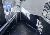 Interior view of a white horse trailer with a divider gate on the left and barred windows along the right wall, black lower panels, and a non-slip dark floor.