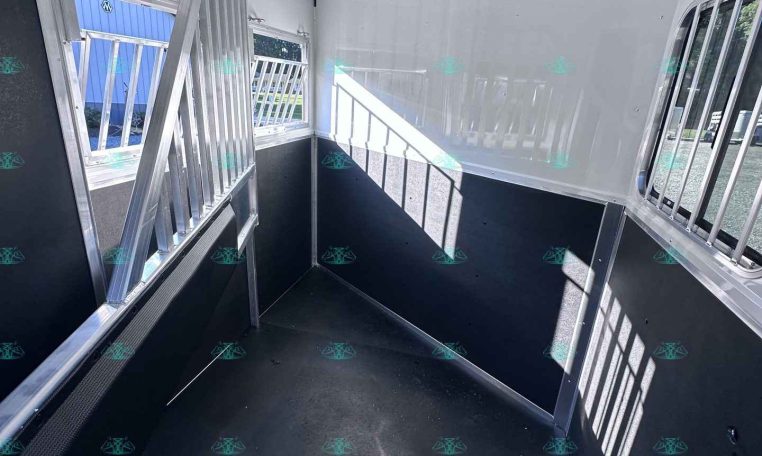 Interior view of a white horse trailer with a divider gate on the left and barred windows along the right wall, black lower panels, and a non-slip dark floor.