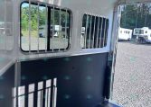 Interior of a white horse trailer with barred windows, a blue lower wall divider, and overhead LED lights inside the stall area