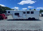 White horse trailer parked on a gravel lot with trees in the background and a bright blue sky with scattered clouds