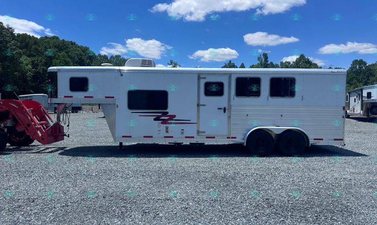 White horse trailer parked on a gravel lot with trees in the background and a bright blue sky with scattered clouds