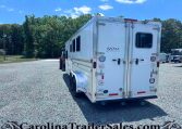 White Exiss horse trailer with dual back doors parked on a gravel lot, trees in the background and a blue sky above