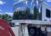 Shiny chrome Exiss trailer parked outdoors under a blue sky with clouds and trees reflected on its surface