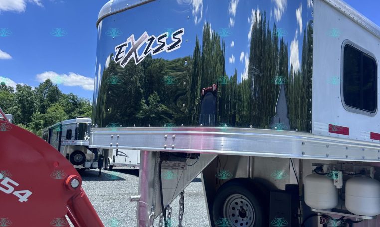 Shiny chrome Exiss trailer parked outdoors under a blue sky with clouds and trees reflected on its surface