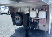 Underbelly of a trailer showing a spare tire, two propane tanks, and a battery box mounted inside the rear area.